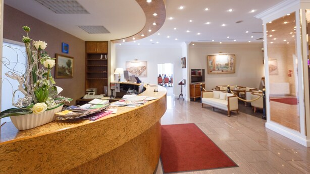 A hotel reception area with a curved reception desk, a red carpet, a sofa, and a painting on the wall. - Hotel Erbprinz (Ludwigslust)