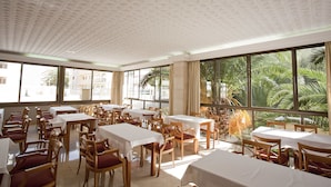 Un espace repas avec des tables et des chaises, de grandes fenêtres offrant une vue sur les palmiers.