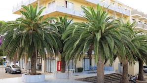 Un immeuble à plusieurs étages doté de balcons, de palmiers et d’une allée piétonne dallée.