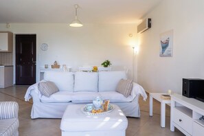 A modern living room with a white sofa, a small table with a tray of snacks, a television, and a painting on the wall.