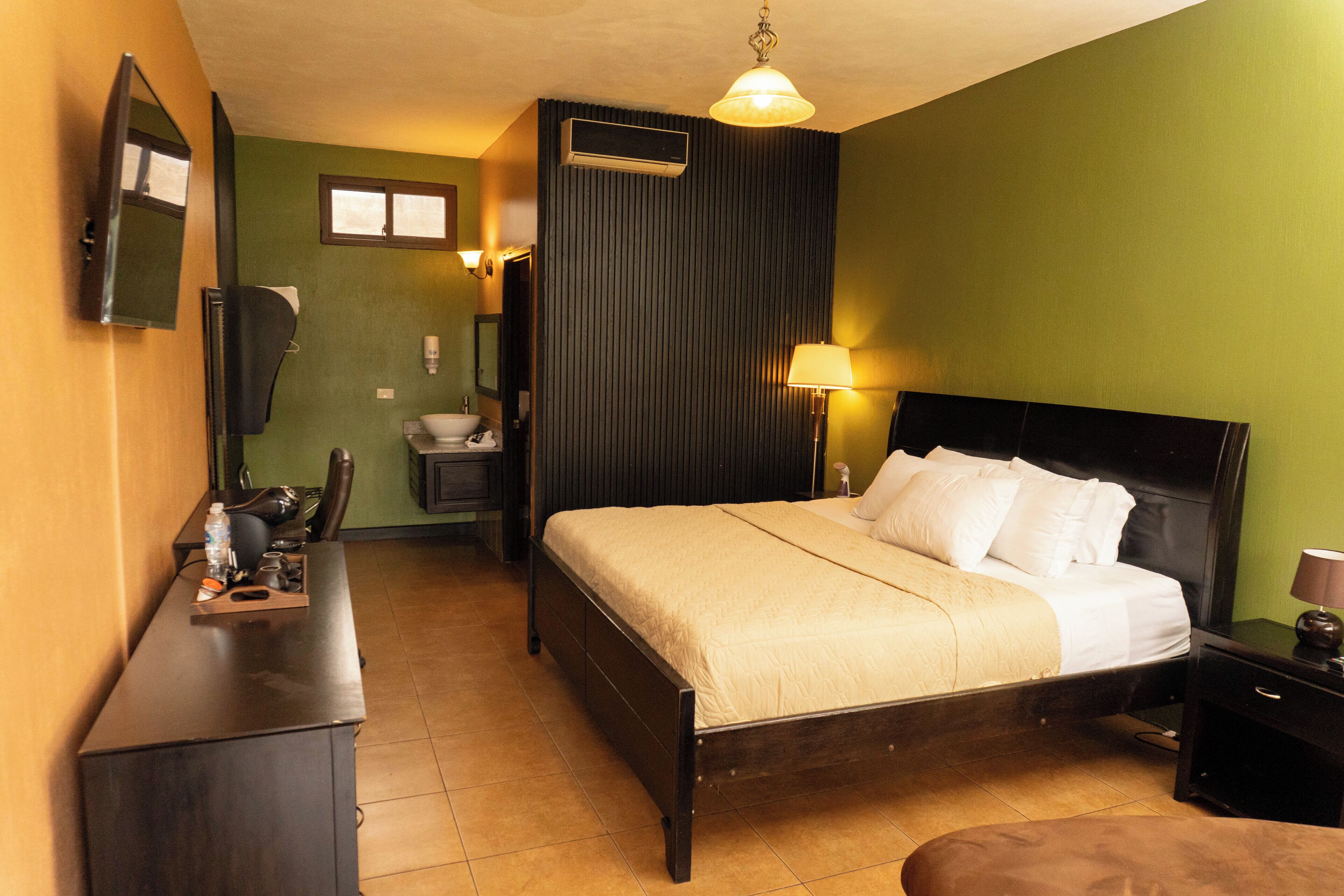 A hotel room with a bed, a desk, a chair, a lamp, and a mirror.