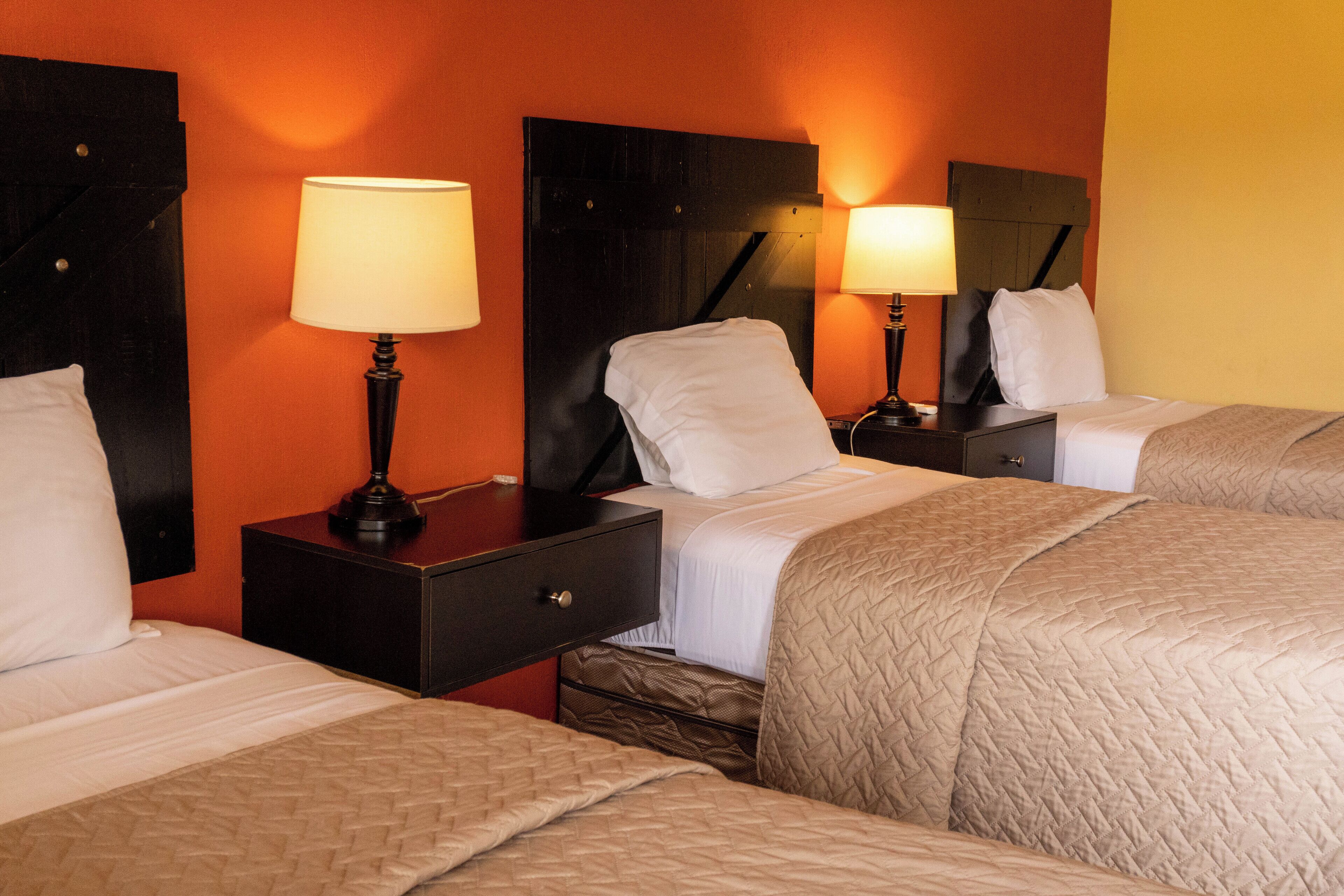 Ein Hotelzimmer mit drei Betten, jeweils mit Kopfteil, Nachttischen und Lampen.