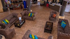 A lobby with multiple seating areas, a reception desk, and a display of products in the background. - Grand Caporal Hotel (Chiquimula)