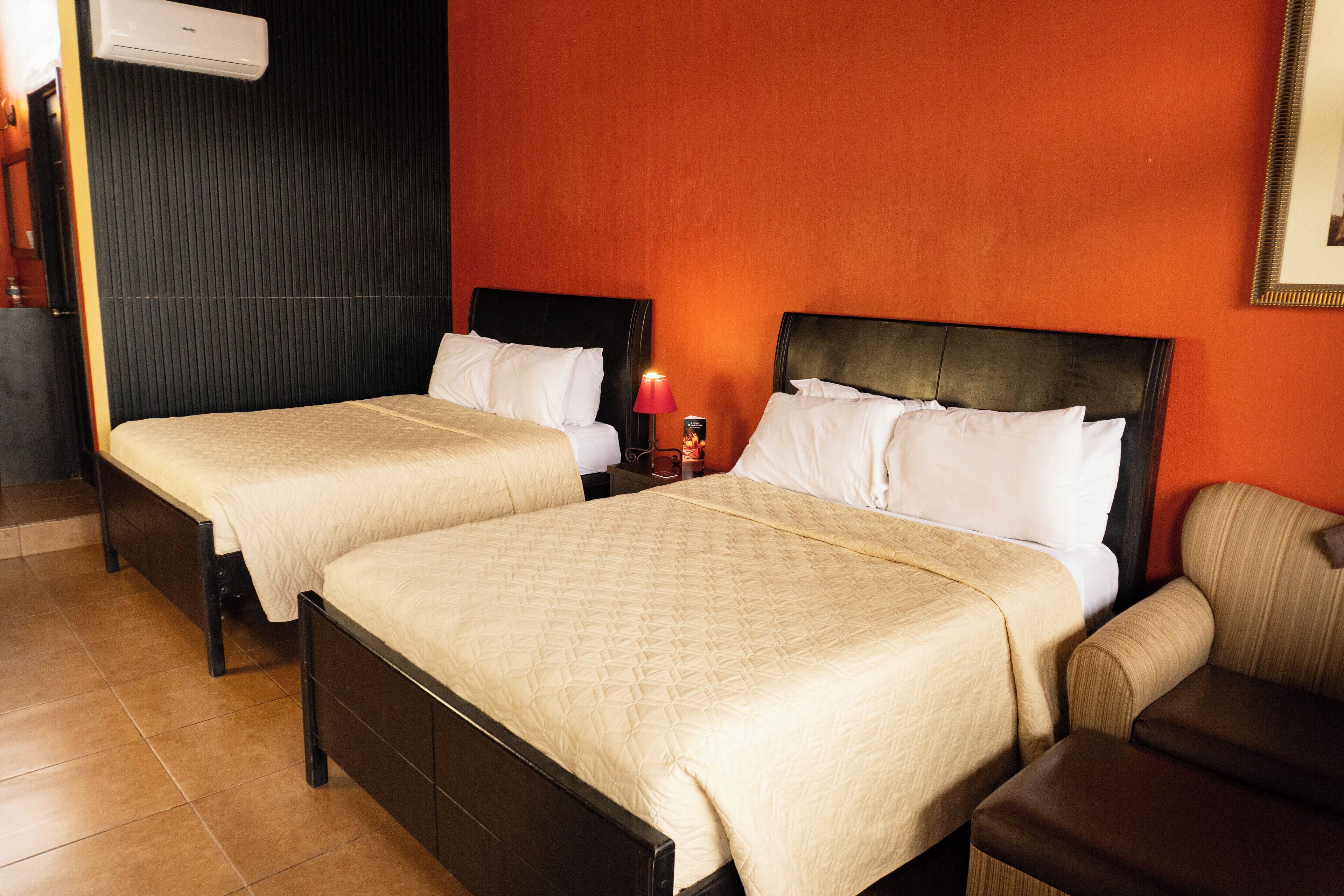 A hotel room with two beds, a nightstand with a lamp, and a chair.