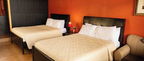 A hotel room with two beds, a nightstand with a lamp, and a chair.