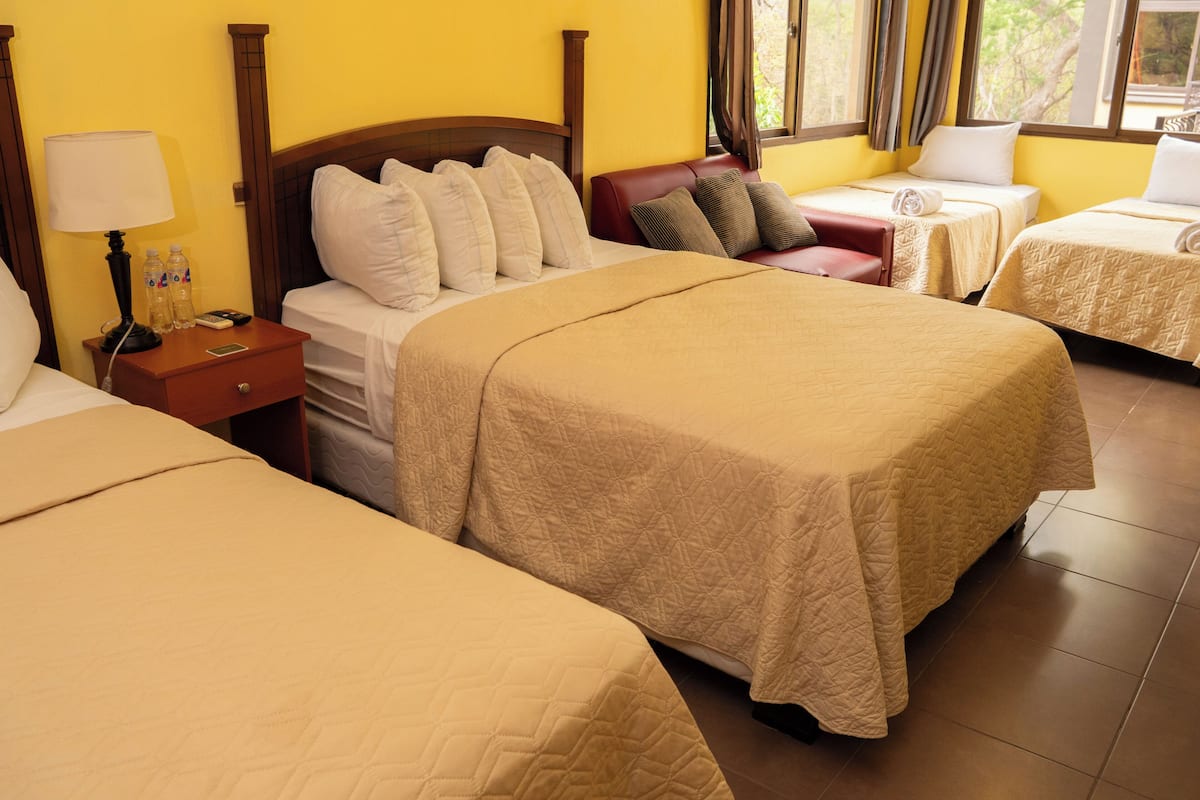 Een hotelkamer met een groot bed, een kleiner bed, een nachtkastje met een lamp en een raam met gordijnen.