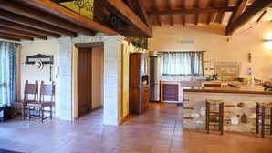 Un salón comedor amplio con cocina, vigas de madera y un detalle de piedra.