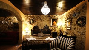 Una habitación con pared de piedra, una cama con colcha de estampado de leopardo, un candelabro y sillones a rayas.