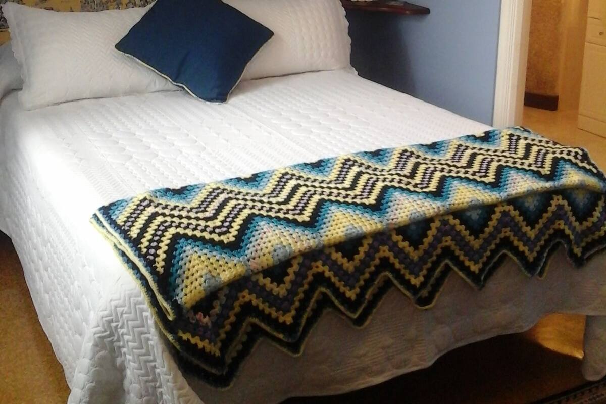 Een bed met een hoofdbord met een patroon, een blauw kussen en een gewatteerd deken.