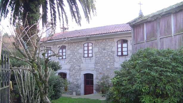 A stone building with a red door and multiple windows, surrounded by greenery and a fence. - Casa Xan de Pena (Vilarmaior)