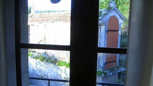 Vista a través de una ventana con balcón, pared de piedra y puerta de madera.
