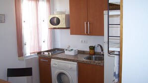 Een kleine keuken met een wasmachine, magnetron en spoelbak.
