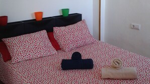 Een net opgemaakt bed met een stippenpatroon, een opgevouwen handdoek en een kleine potplant op een plank erboven.