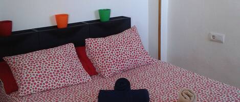 Un lit bien fait, avec un couvre-lit à pois, une serviette pliée et une petite plante en pot posée sur une étagère au-dessus.