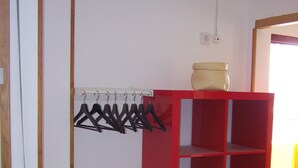 Een rode wandplank met verschillende vakken, een wit, aan de muur bevestigd kledingrek met zwarte hangers en een houten deurkozijn.