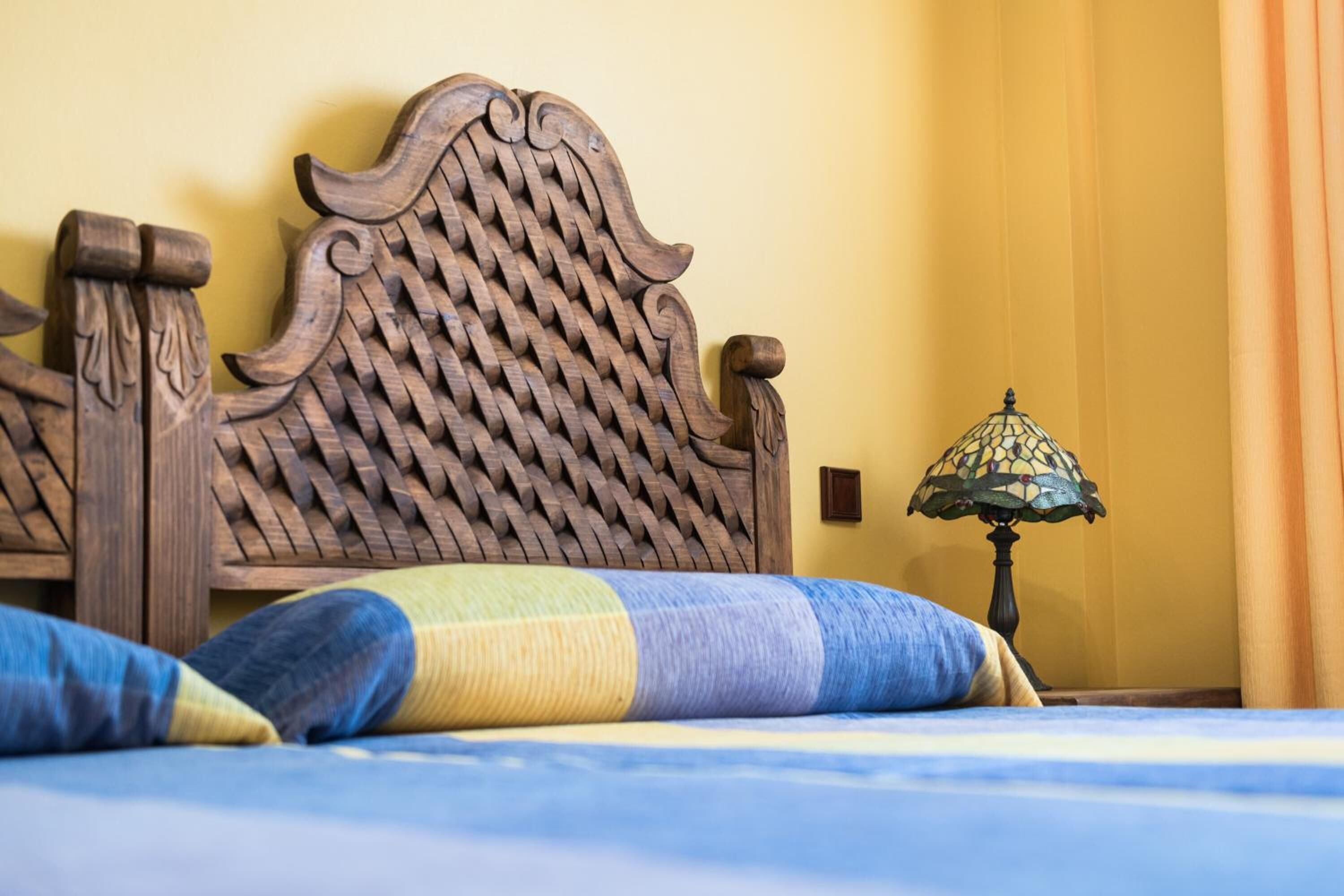 A bed with a wooden headboard, a patterned pillow, and a table lamp.