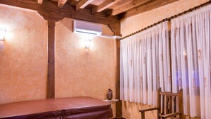 A spa room with a wooden bench, a chair, a wall-mounted heater, and a window with curtains.