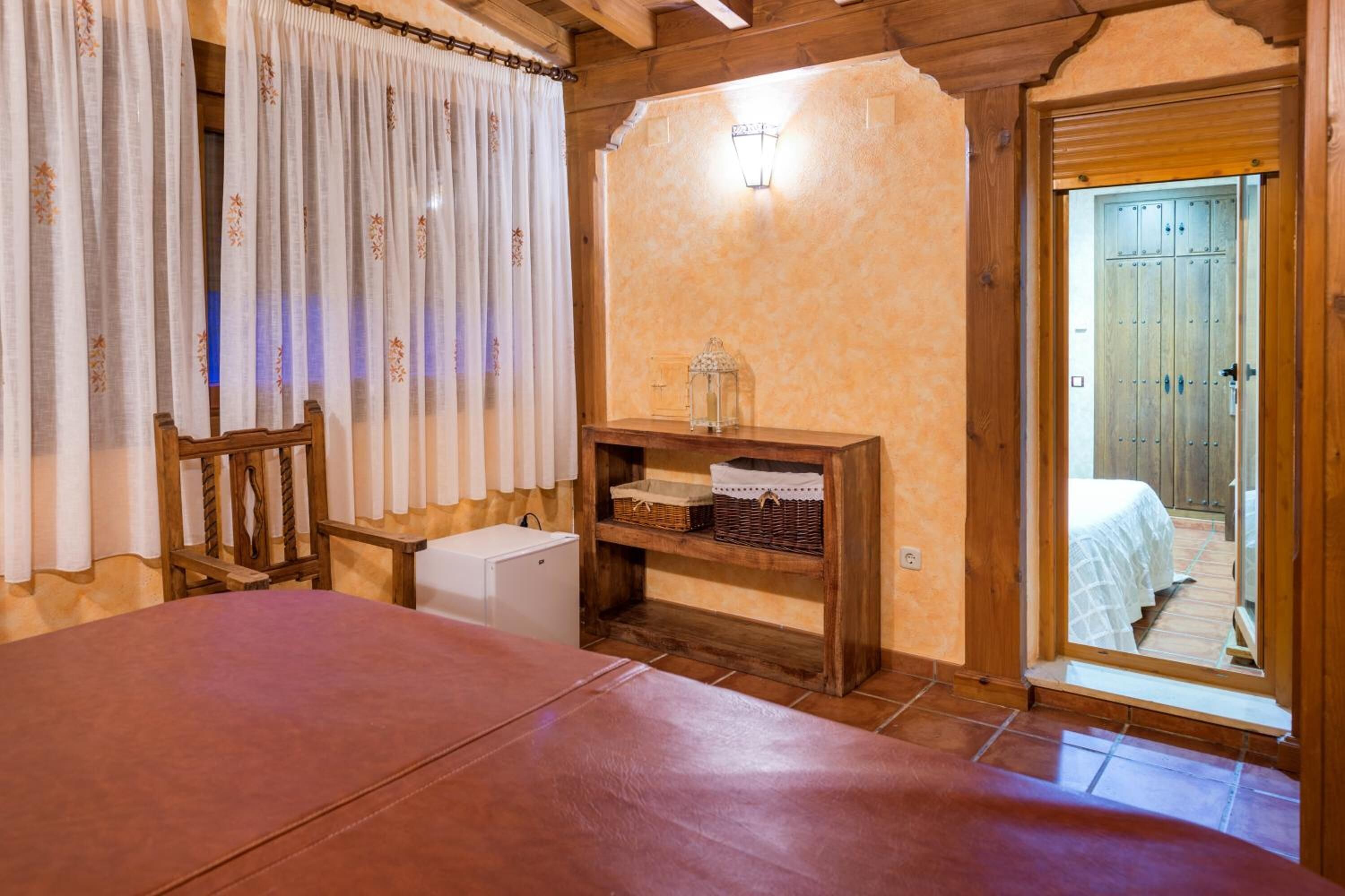 A cozy room with a wooden table, a small white cabinet, a shelf with baskets, and a door leading to a bedroom.