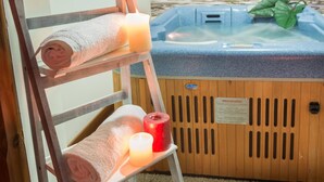 Een houten stoel met opgerolde handdoeken en kaarsen, een hottub met een houten paneel en een bordje, en een plant op de hottub.