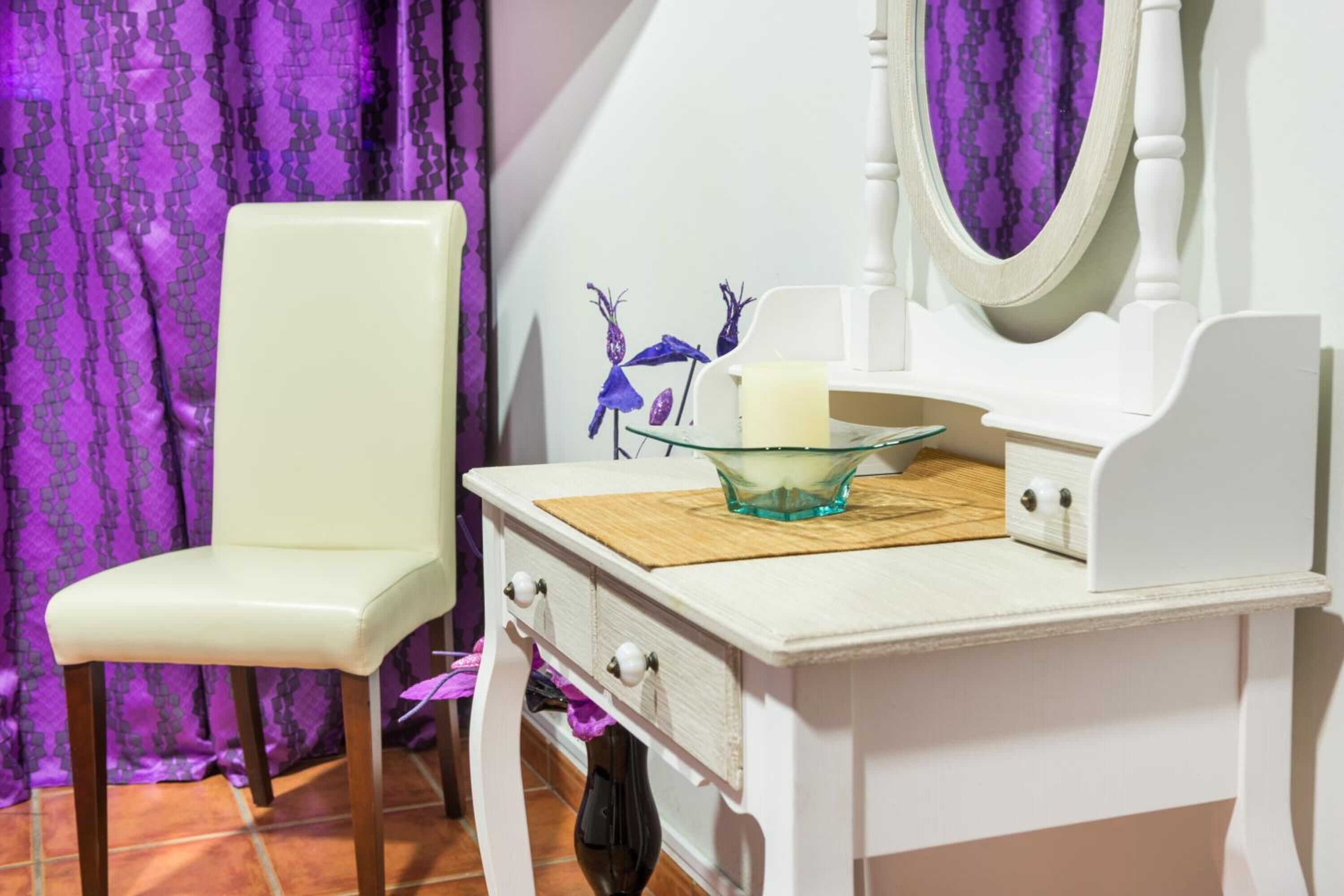A white vanity with a mirror, a glass bowl, and a candle on a wooden tray.
