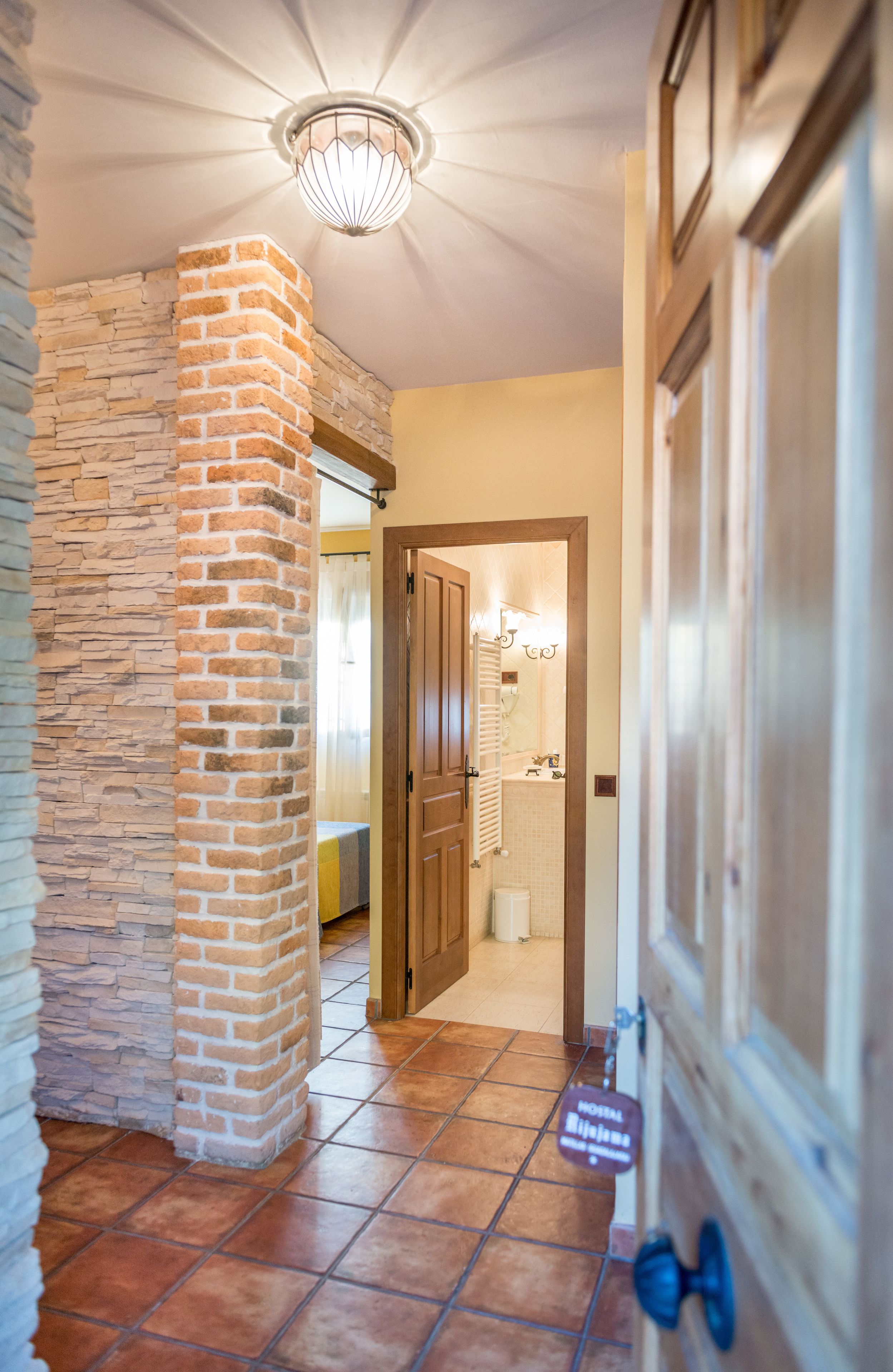 Un pasillo con un pilar de ladrillo, una puerta de madera y un letrero que indica el tipo de habitación.