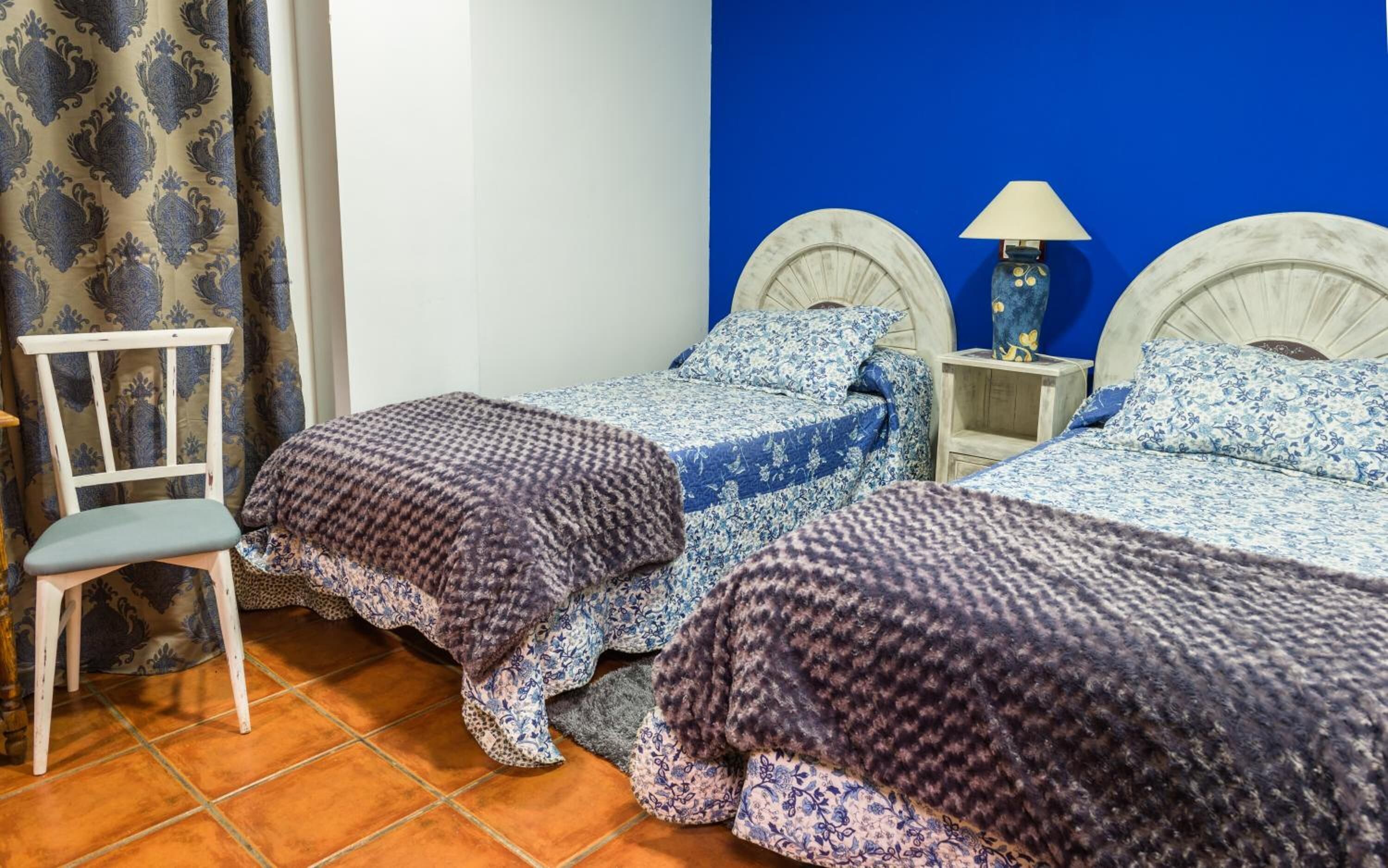 Una habitación con dos camas, una silla y una mesita de noche con lámpara.