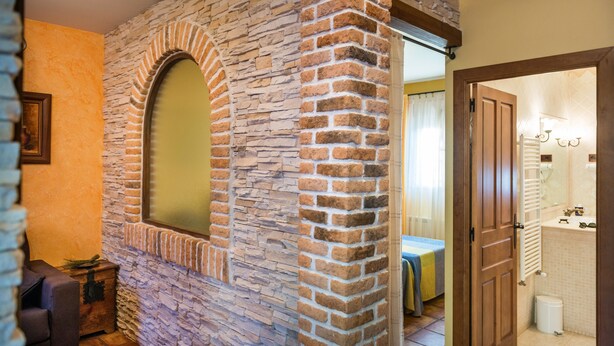 A room with a stone wall, a wooden door, and a bed with a blue and yellow bedspread.