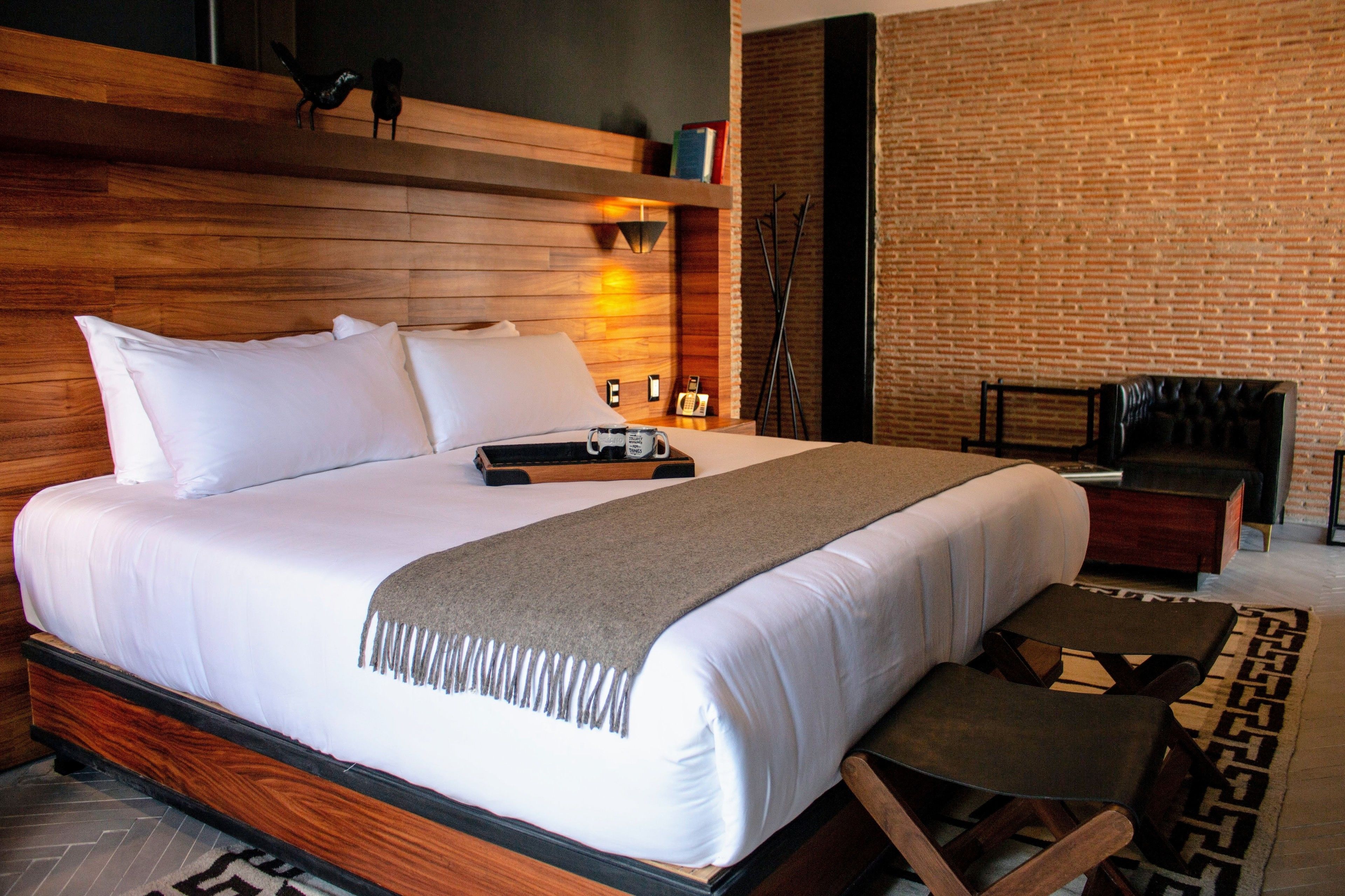 Una habitación de hotel moderna con una cama grande, cabecero de madera y una pared de ladrillo.