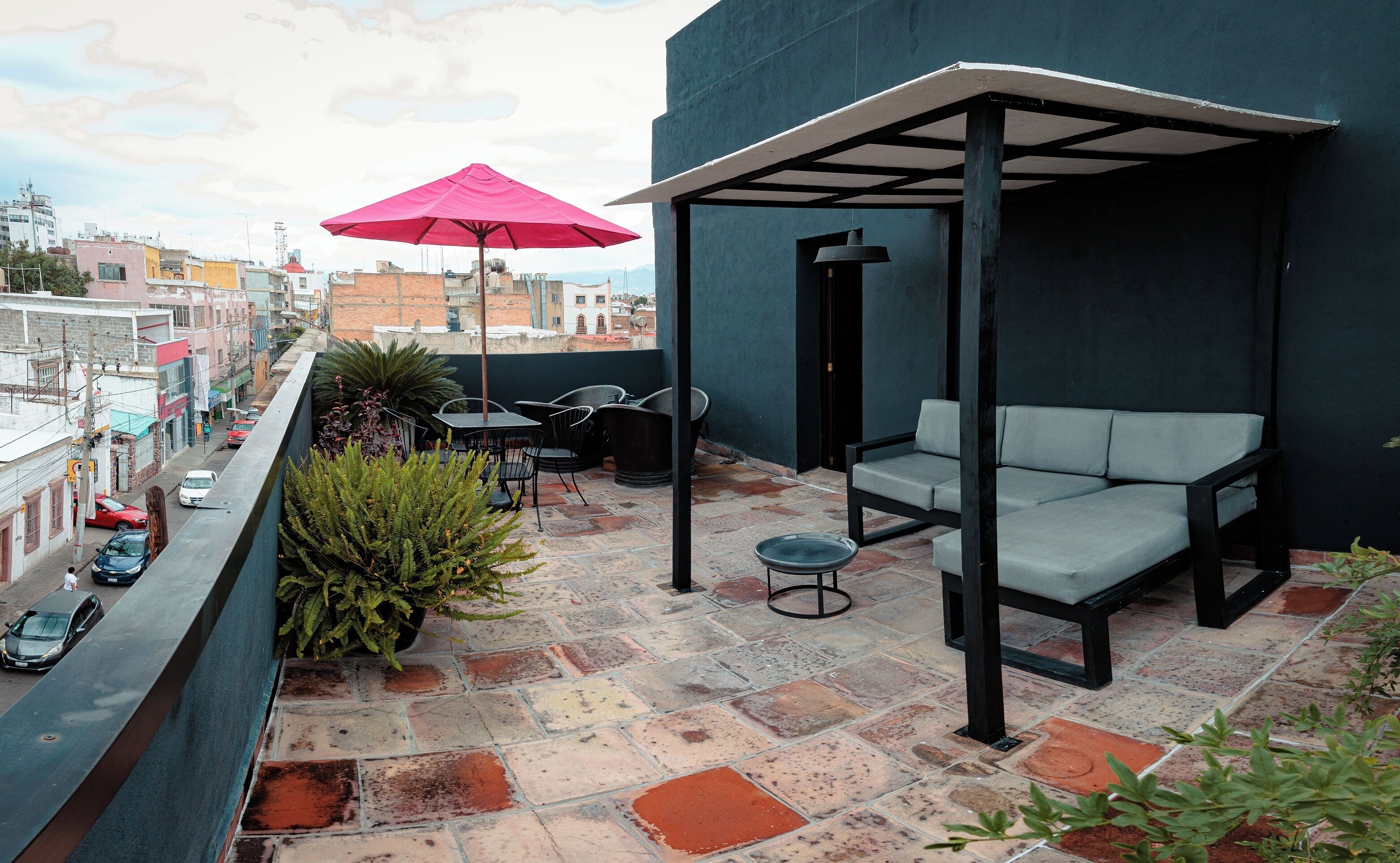 Une terrasse sur le toit, avec un espace salon, une table et un parasol rouge.