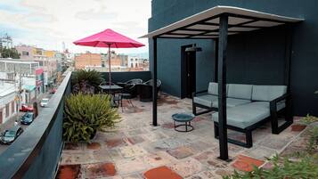 Une terrasse sur le toit, avec un espace salon, une table et un parasol rouge.
