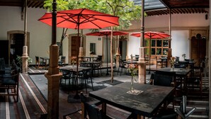 An outdoor cafe with tables and chairs under red umbrellas, surrounded by greenery and a wooden structure. - Elena de Cobre, Leon, a Member of Design Hotels (León)
