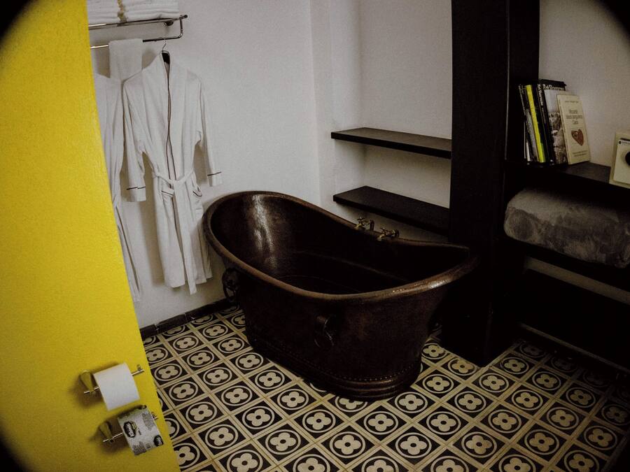 Un baño con una bañera de patas de león antigua, un perchero con toallas blancas, una estantería con libros y baldosas de suelo estampadas.