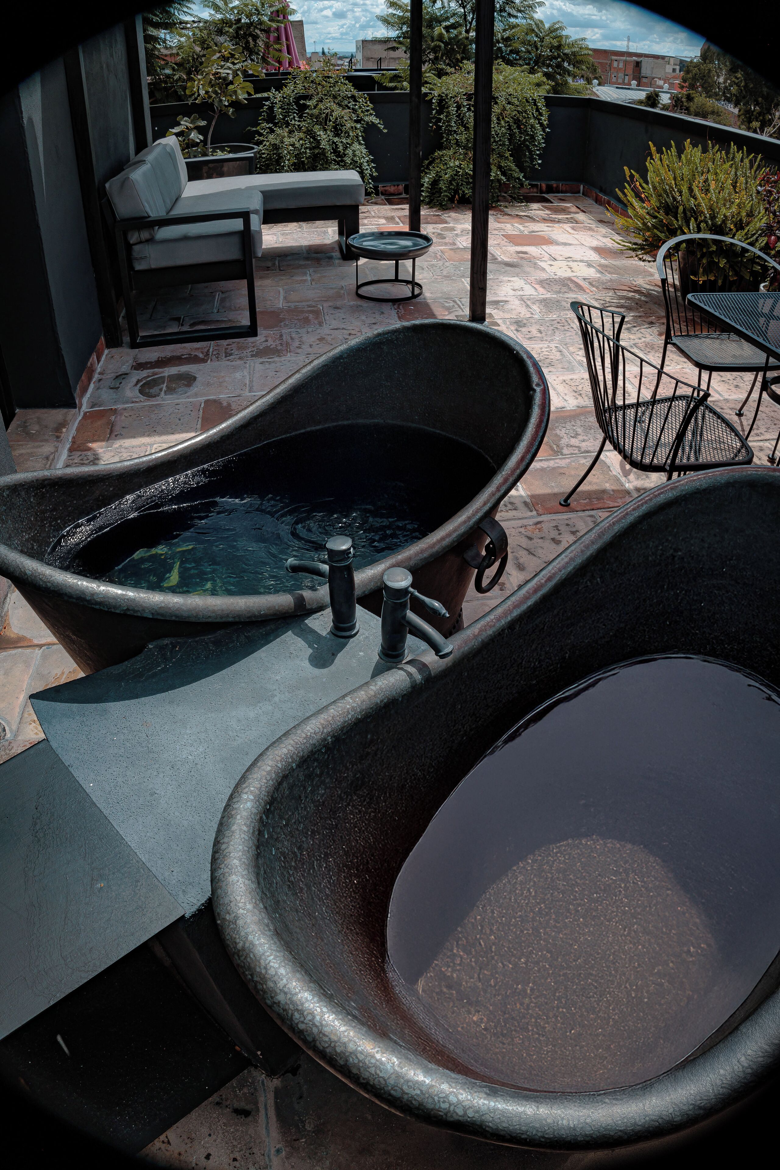 A rooftop terrace with a black bathtub, a lounge chair, and a dining table.