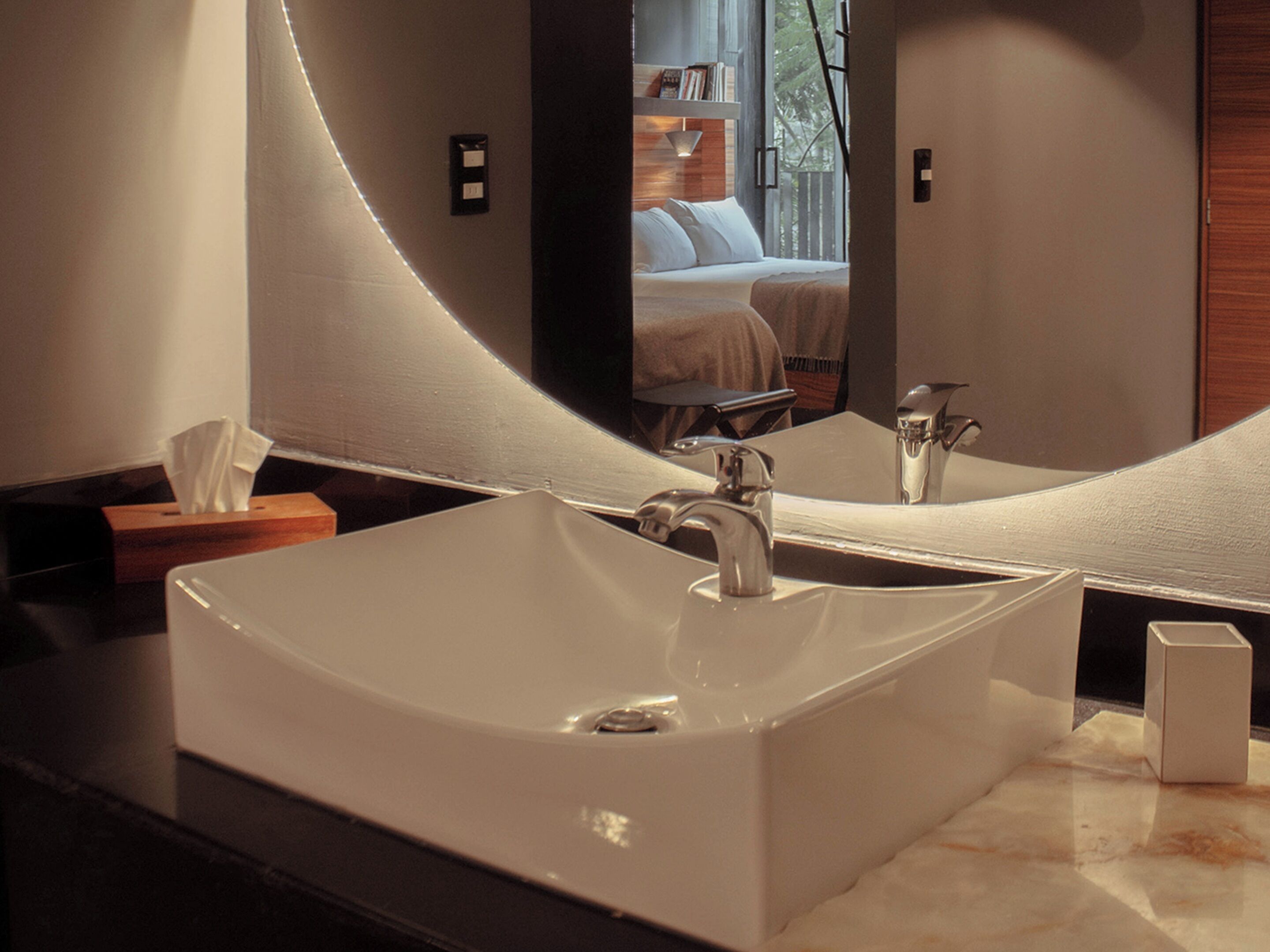 A modern bathroom with a large rectangular sink, a mirror, and a wooden side table with a tissue box.