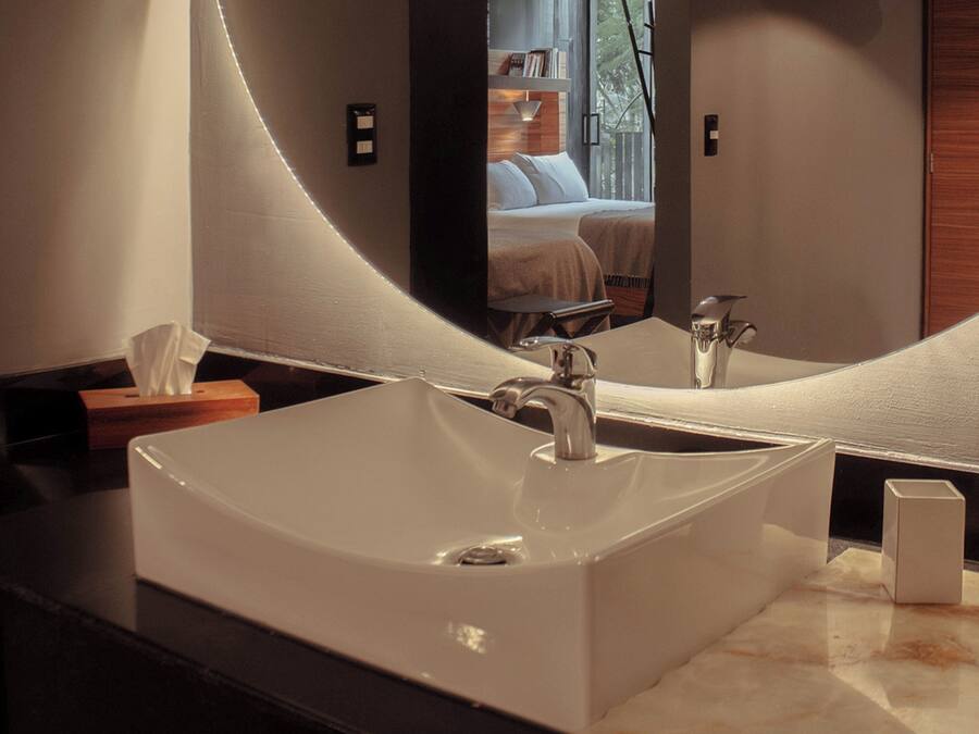 A modern bathroom with a large rectangular sink, a mirror, and a wooden side table with a tissue box.