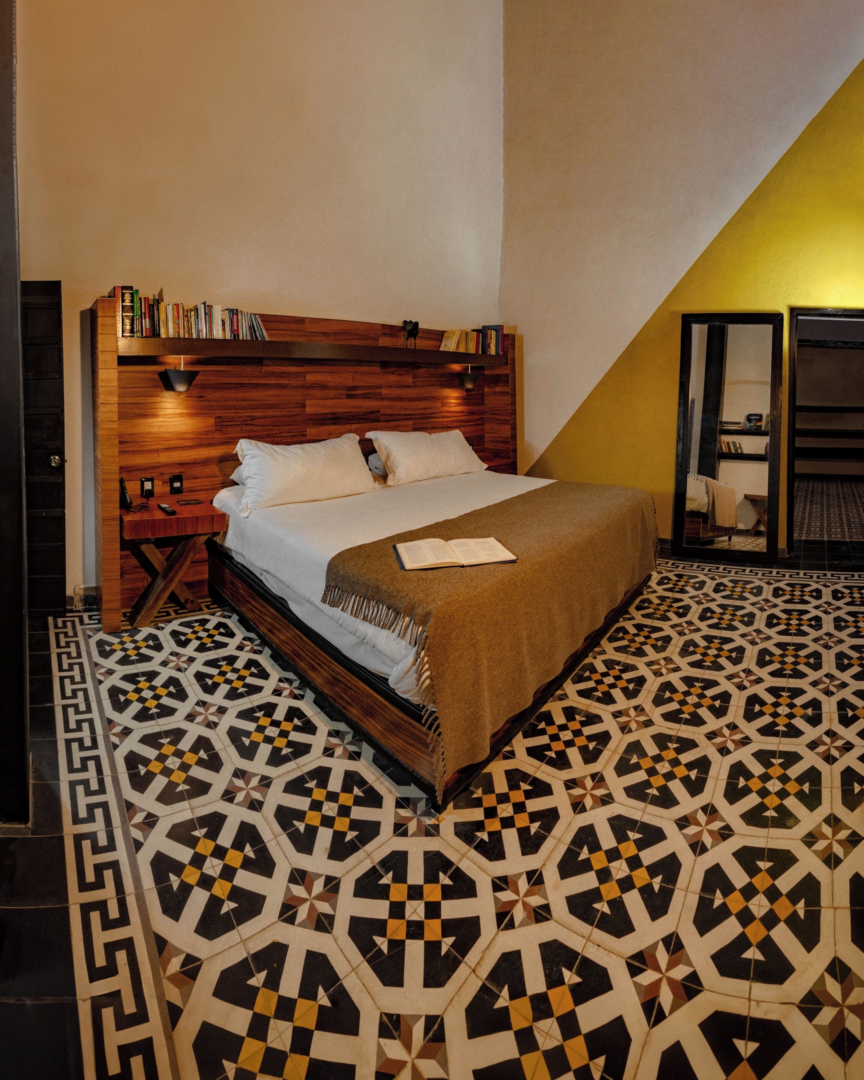 A bedroom with a wooden headboard, a patterned floor, and a bedside table with books.