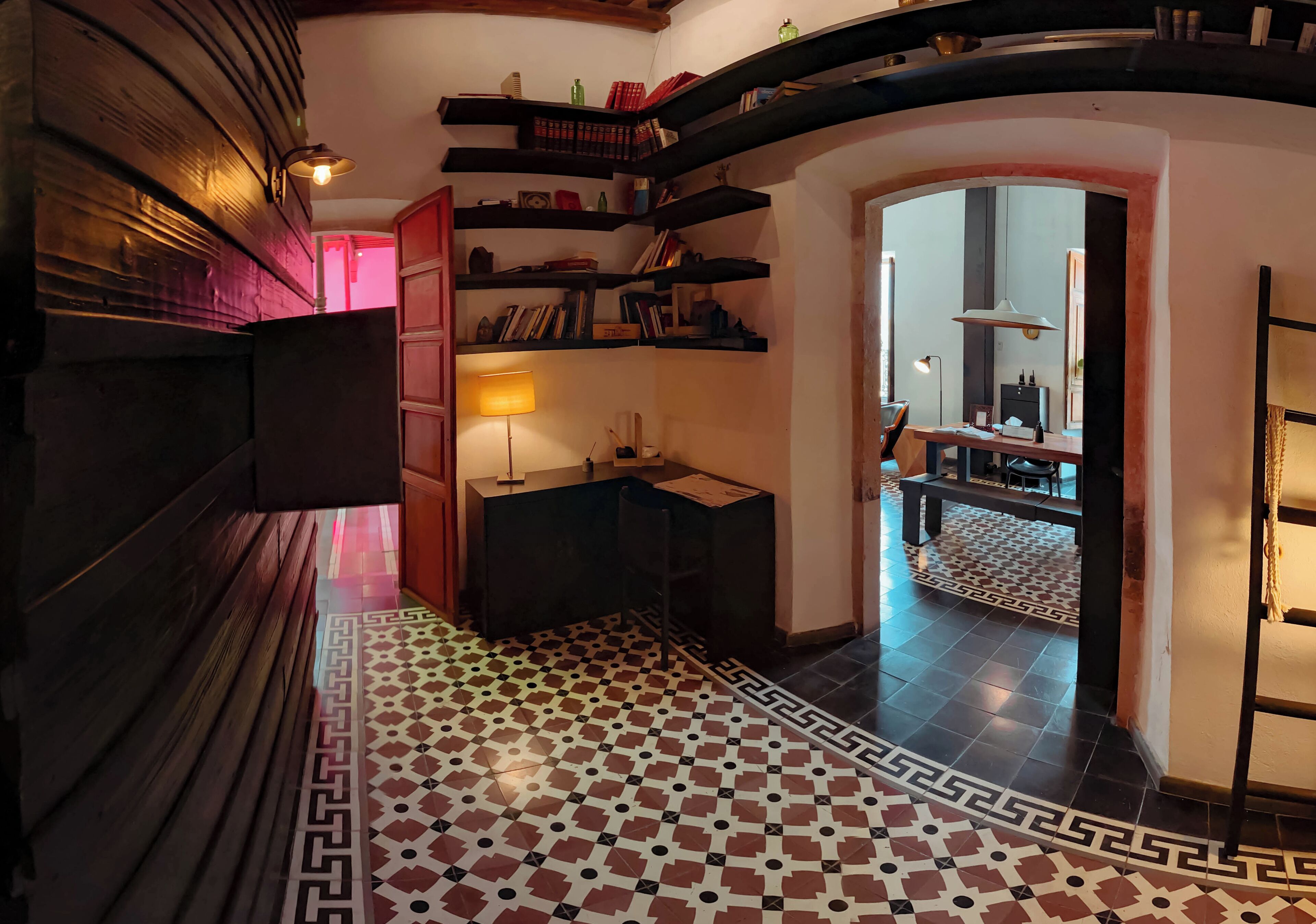 Un couloir avec un sol à carreaux, des étagères à livres, un bureau et une lampe.