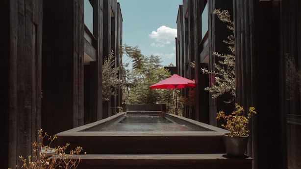 A narrow, covered walkway with a red umbrella, flanked by tall buildings and trees. - Elena de Cobre, Leon, a Member of Design Hotels (León)