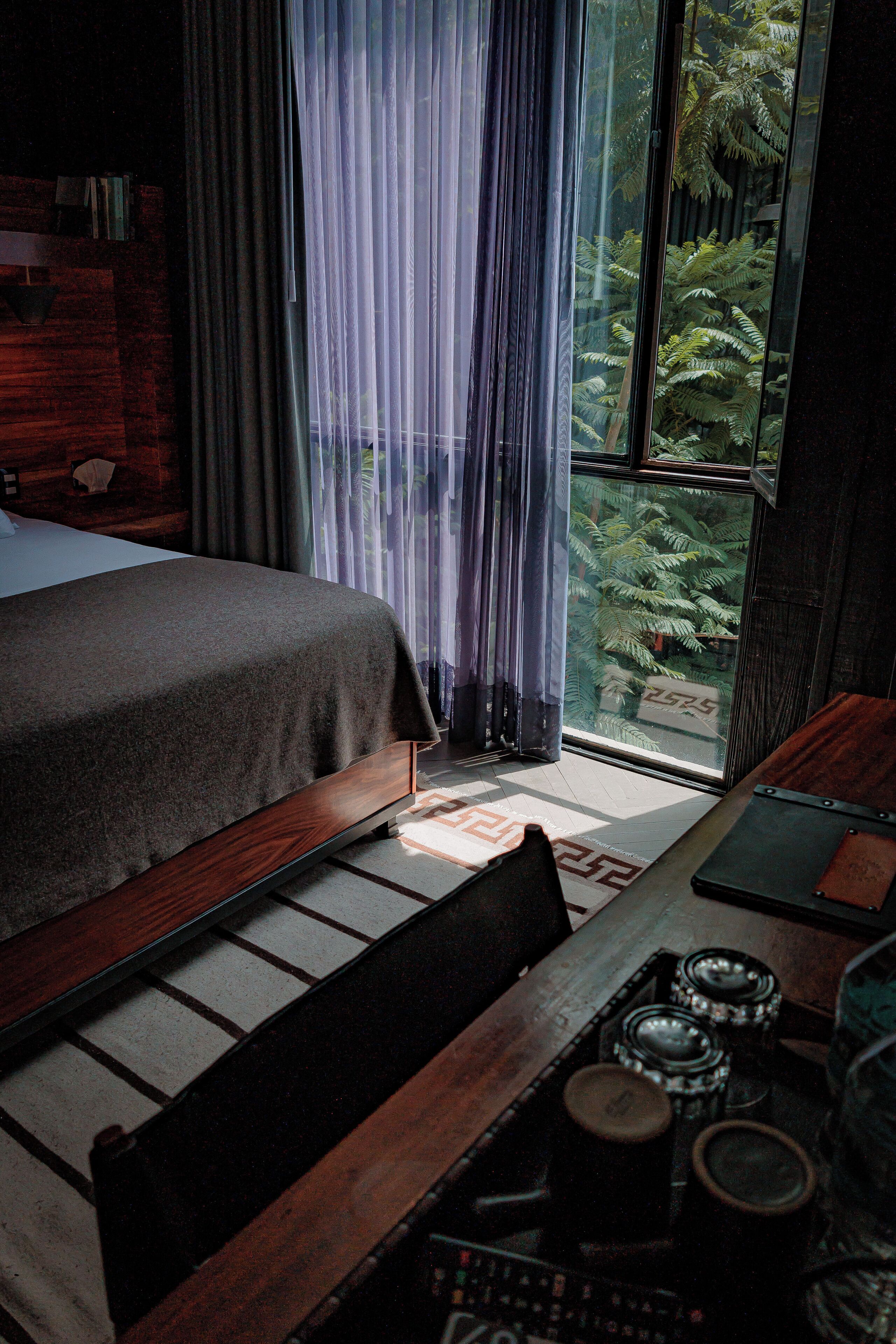 Quarto com cama, escrivaninha de madeira e vista para uma floresta pela janela.