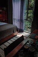 Quarto com cama, escrivaninha de madeira e vista para uma floresta pela janela.