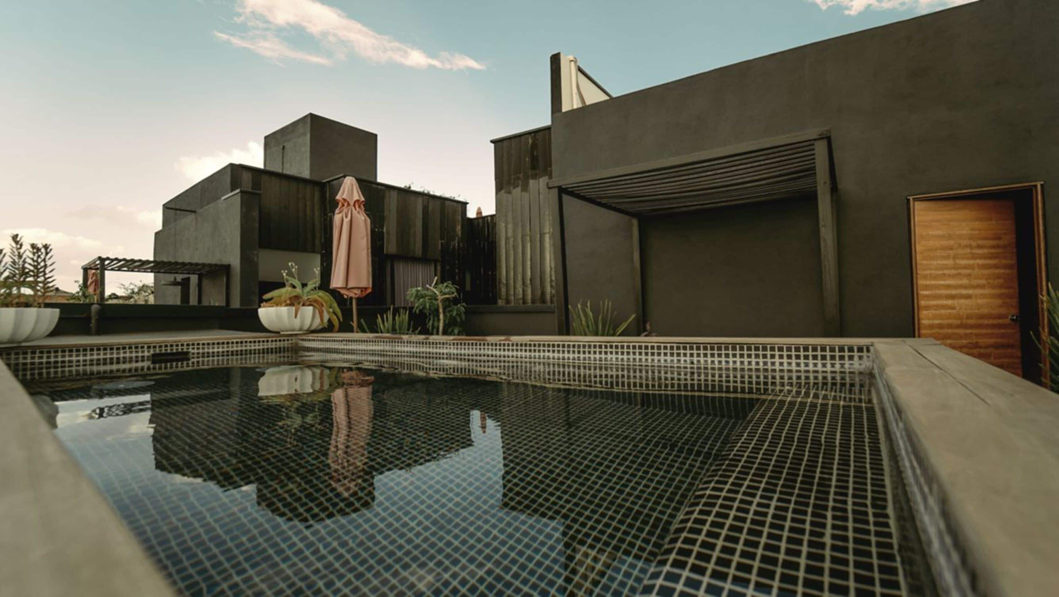 Un edificio moderno con piscina, plantas en macetas y una puerta de madera.