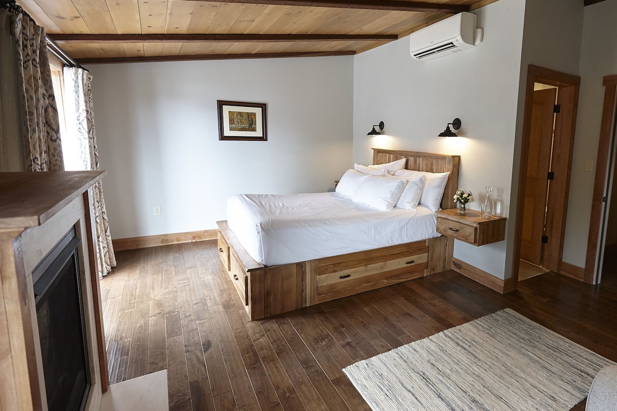 A bedroom with a wooden bed, bedside tables, a fireplace, and a framed picture on the wall.