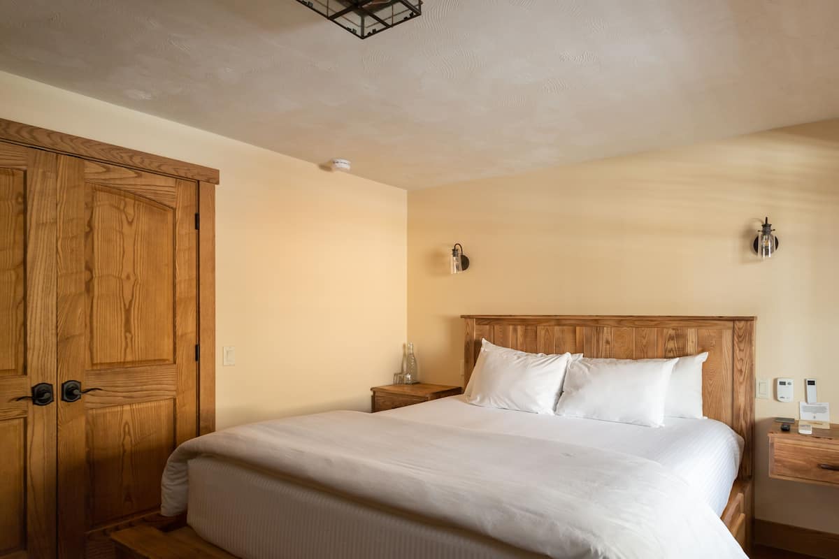 A neatly made bed in a room with wooden furniture, a wooden wardrobe, and a bedside table with a lamp.
