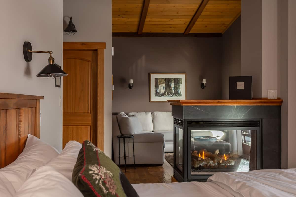 A bedroom with a wooden ceiling, a fireplace, a sofa, and a bed with white bedding.