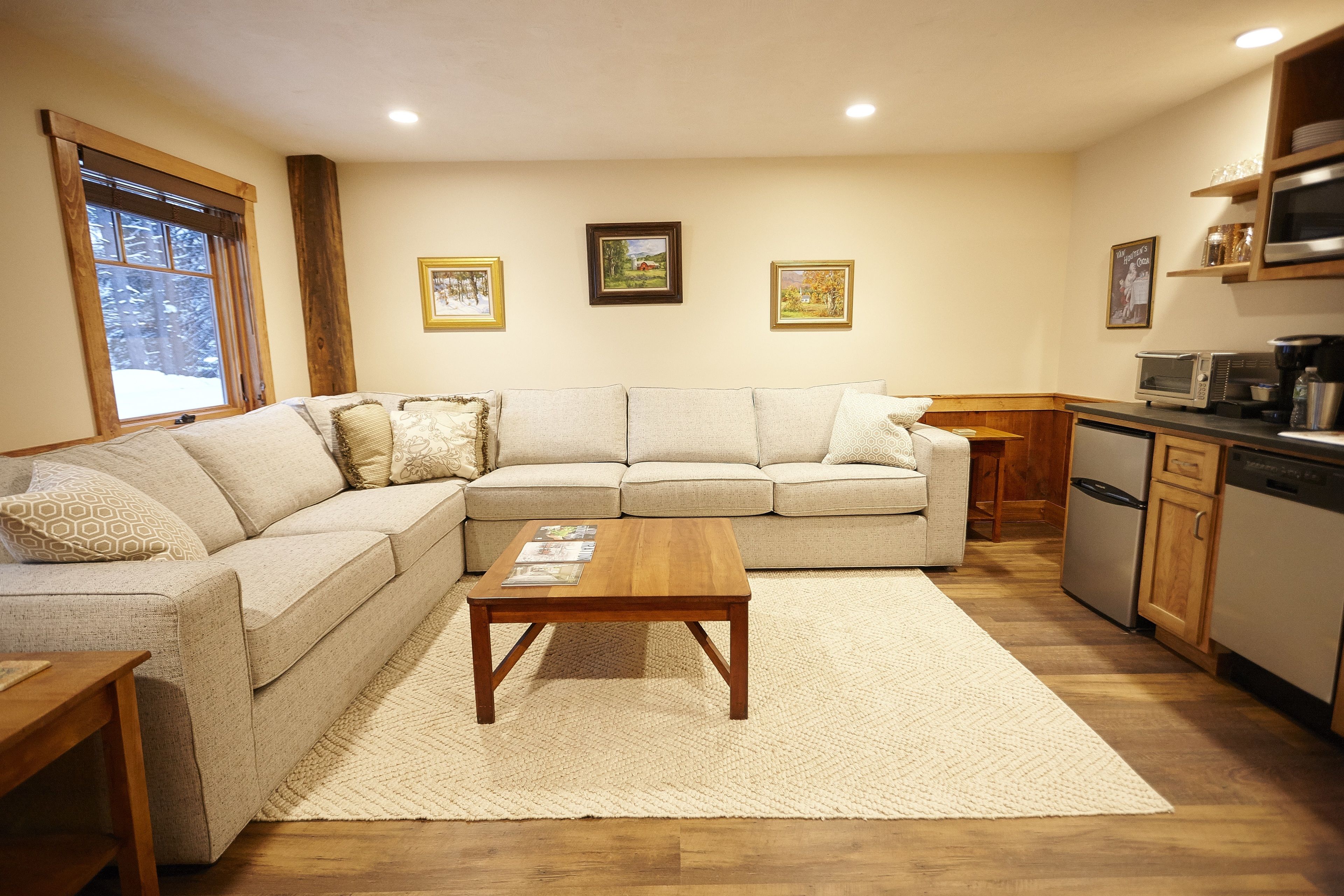 A living room with a sectional sofa, a wooden coffee table, and a kitchen area with appliances.