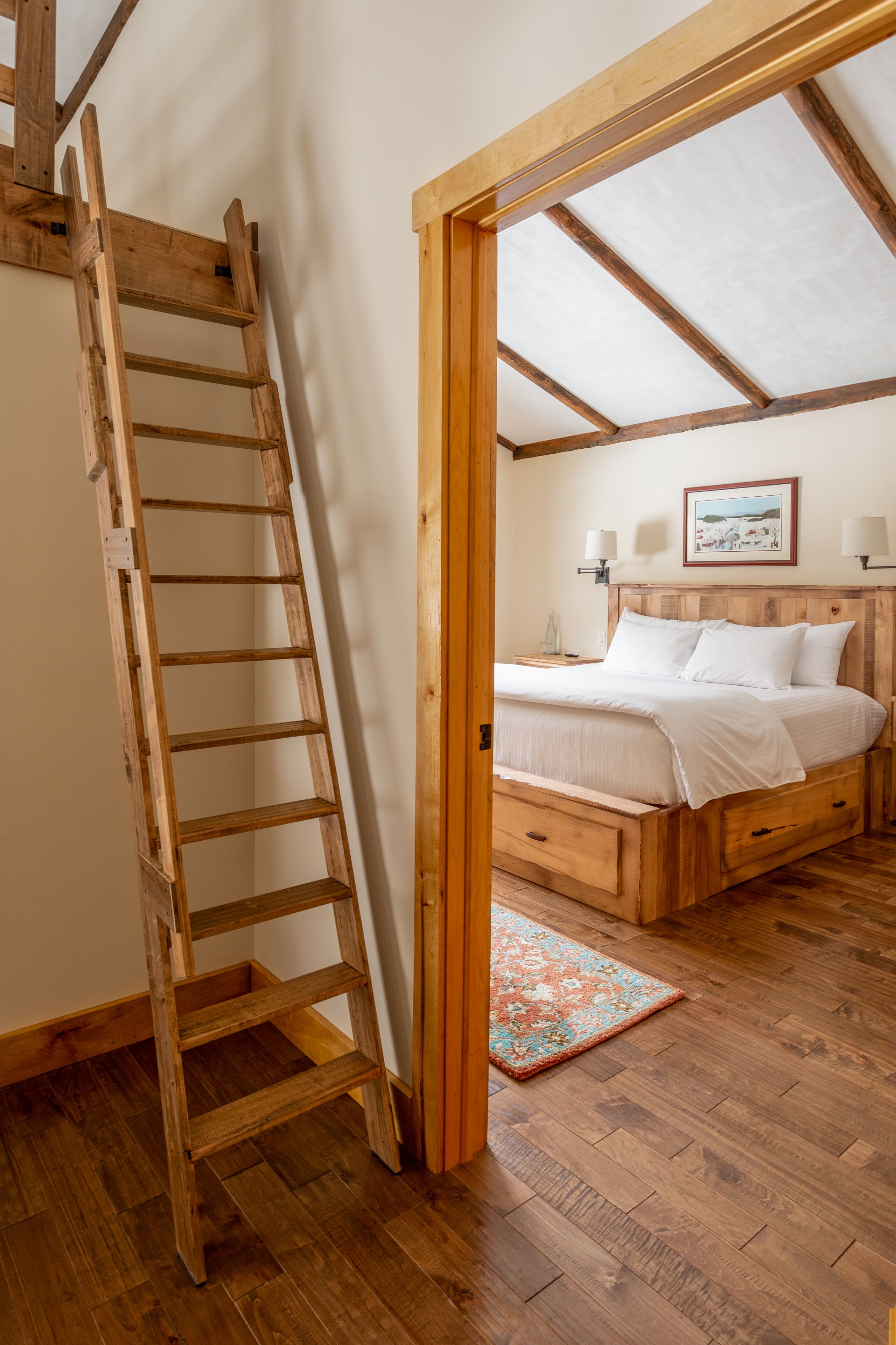 A bedroom with a wooden ladder, a bed with white linens, a wooden headboard, and a wooden floor.