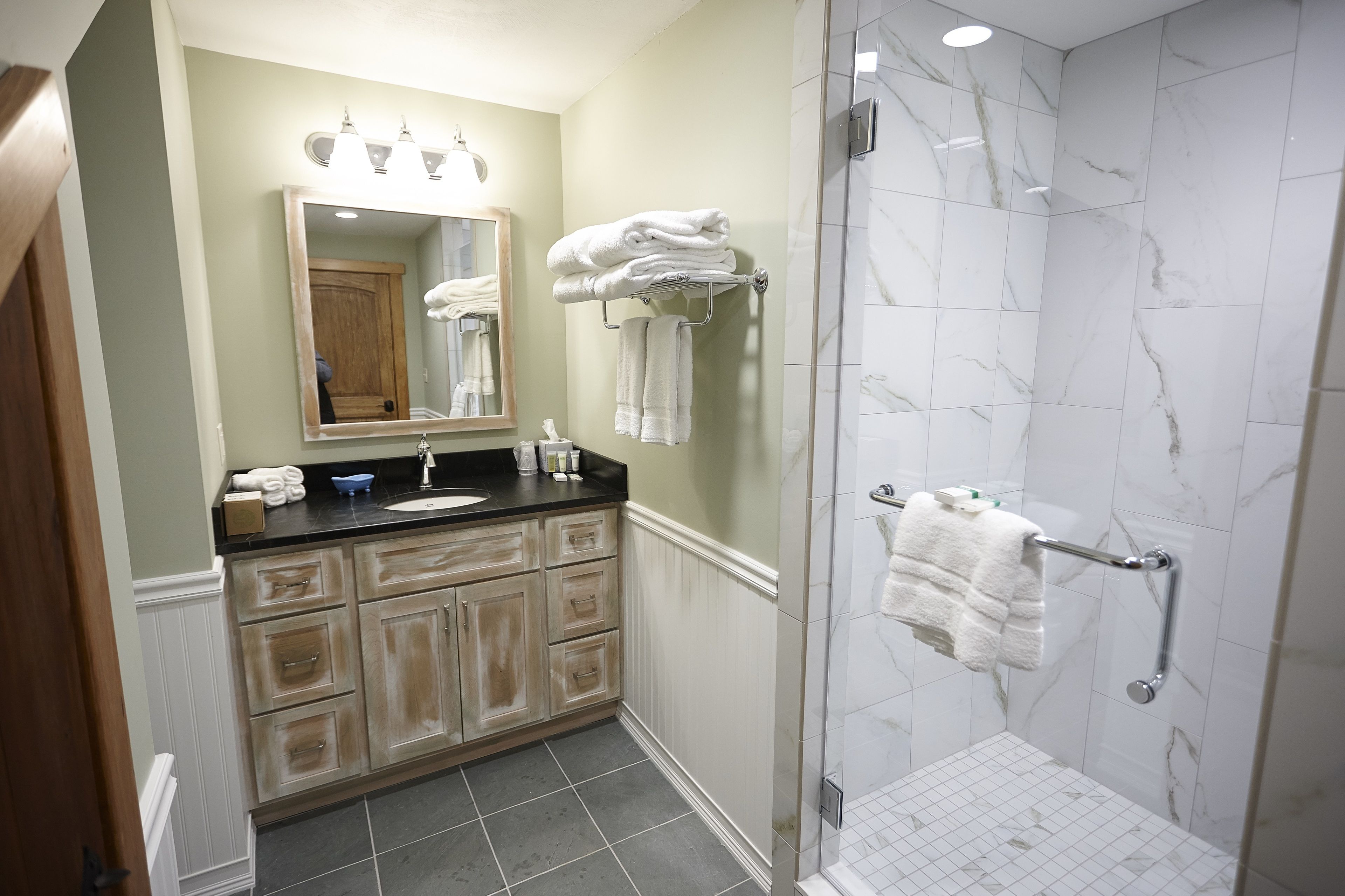A bathroom with a sink, mirror, towel rack, and shower area.