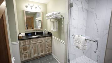 A bathroom with a sink, mirror, towel rack, and shower area.