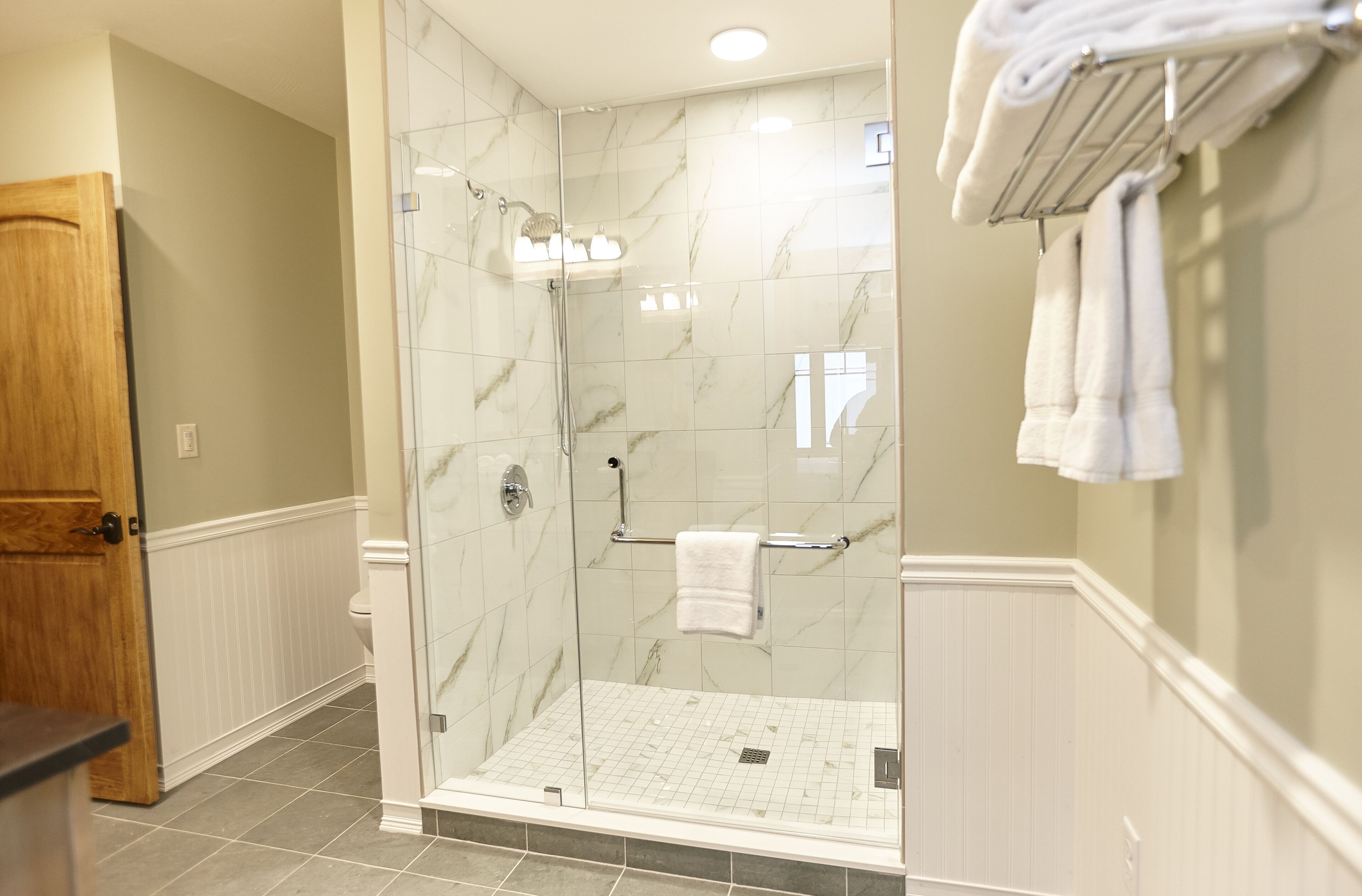 A modern bathroom with a glass-enclosed shower, white tiled walls, and a wooden door.