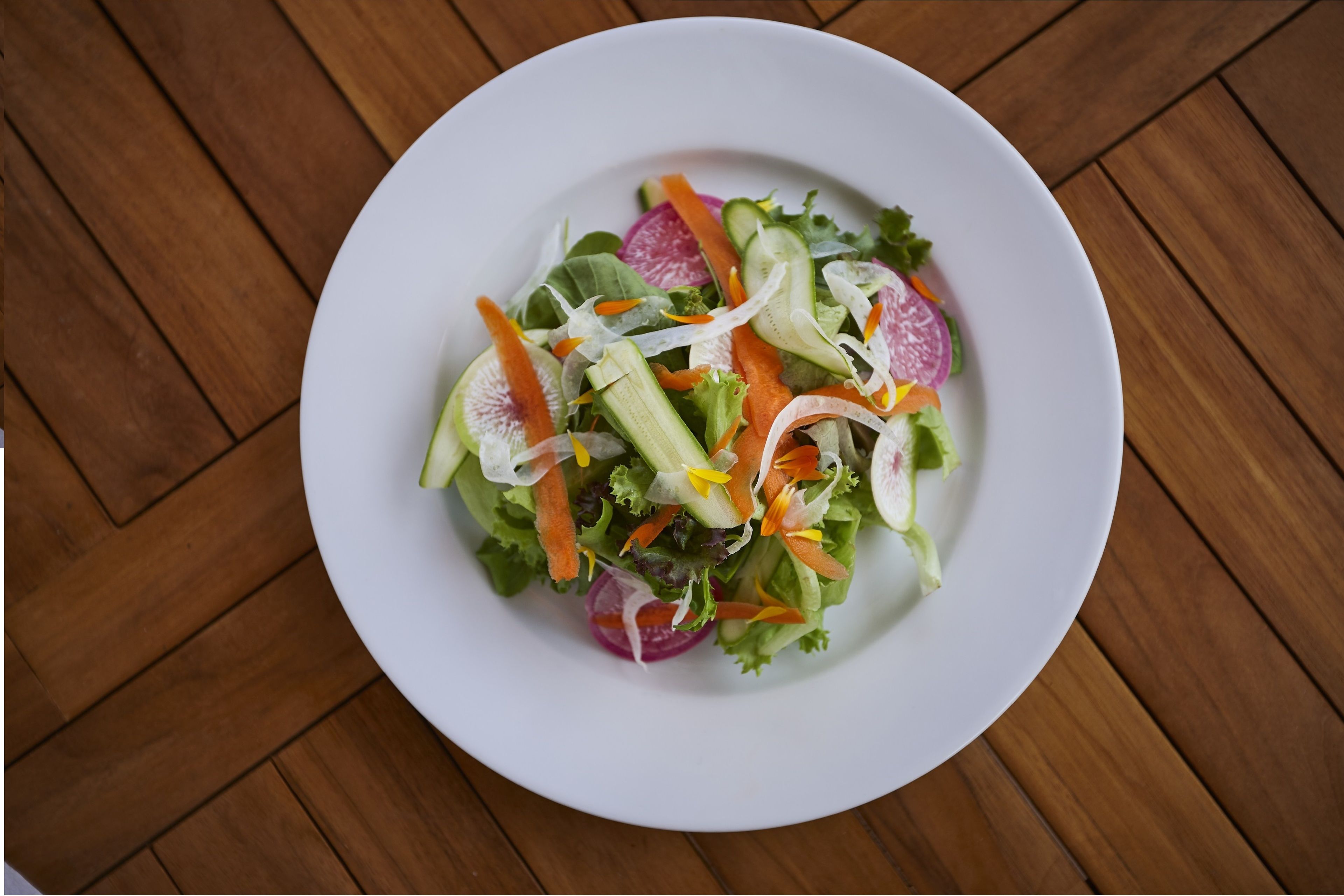 A white plate with a salad on a wooden table.